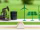 Fossil fuel vs renewable / future clean alternative energy concept : Petroleum pumpjack, crude oil drum barrel, solar panel, green leaf battery, wind turbine on a wood balance scale in equal position.